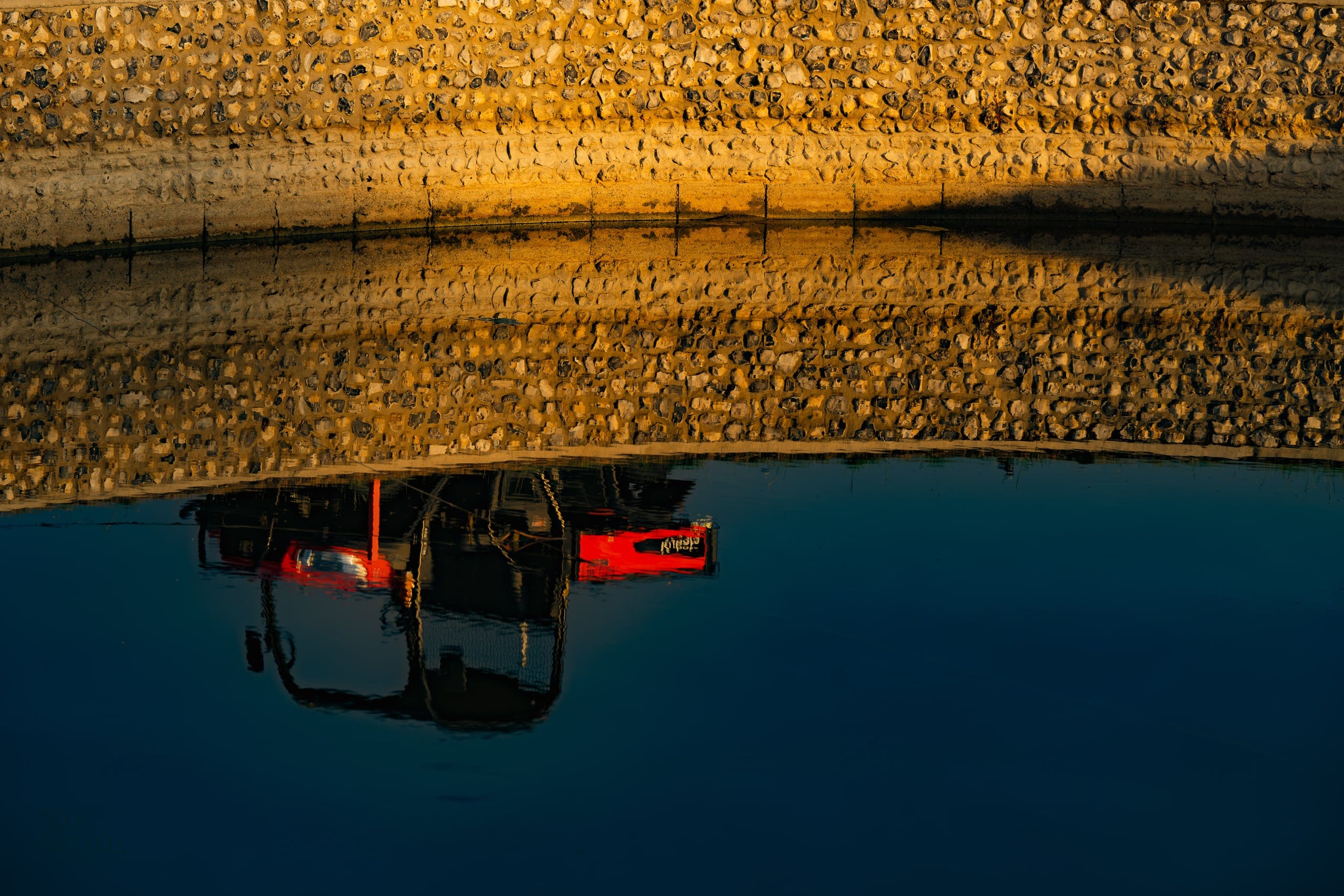 A golf buggy and stone-lined bank reflected in still water