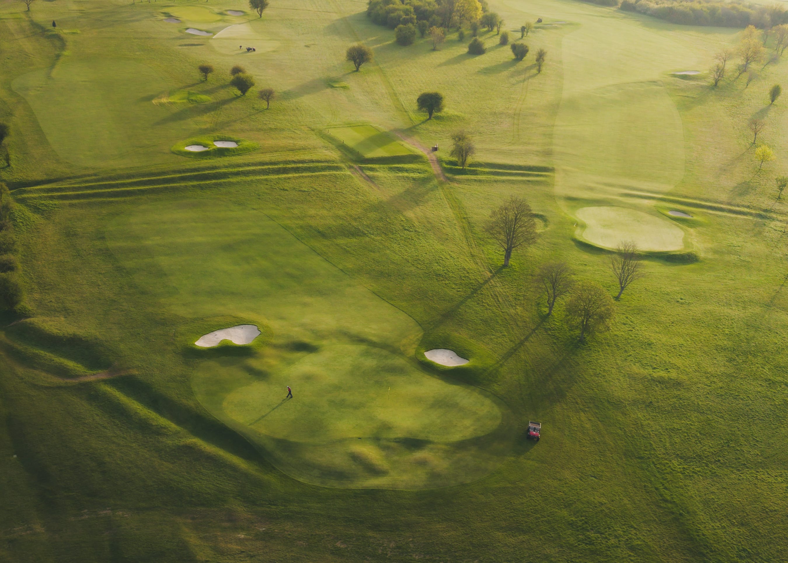 A greenkeeper driving a mower toward camera, hood up against the morning cold