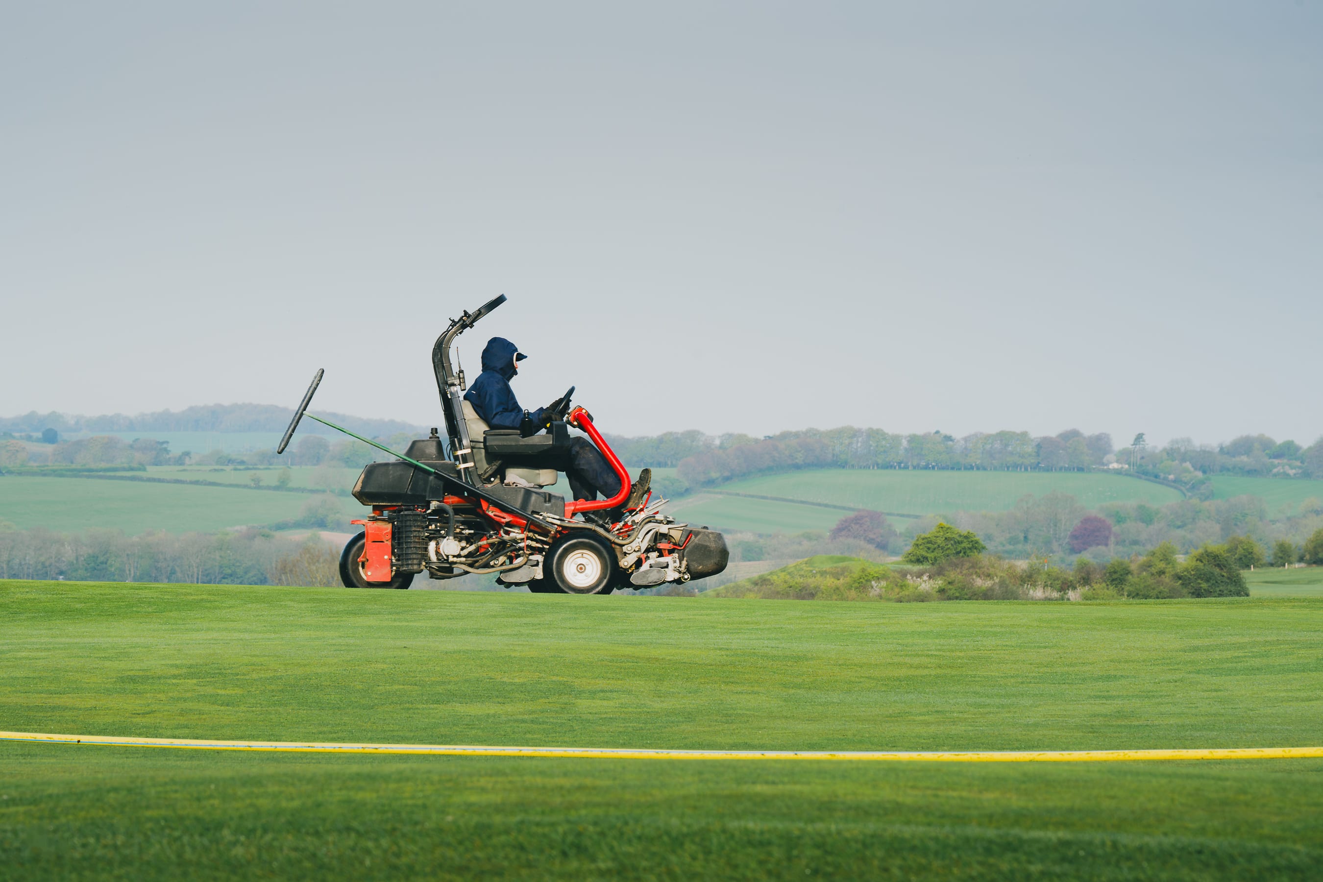 A greenkeeper on a triple mower cutting a fairway, the Hampshire countryside beyond
