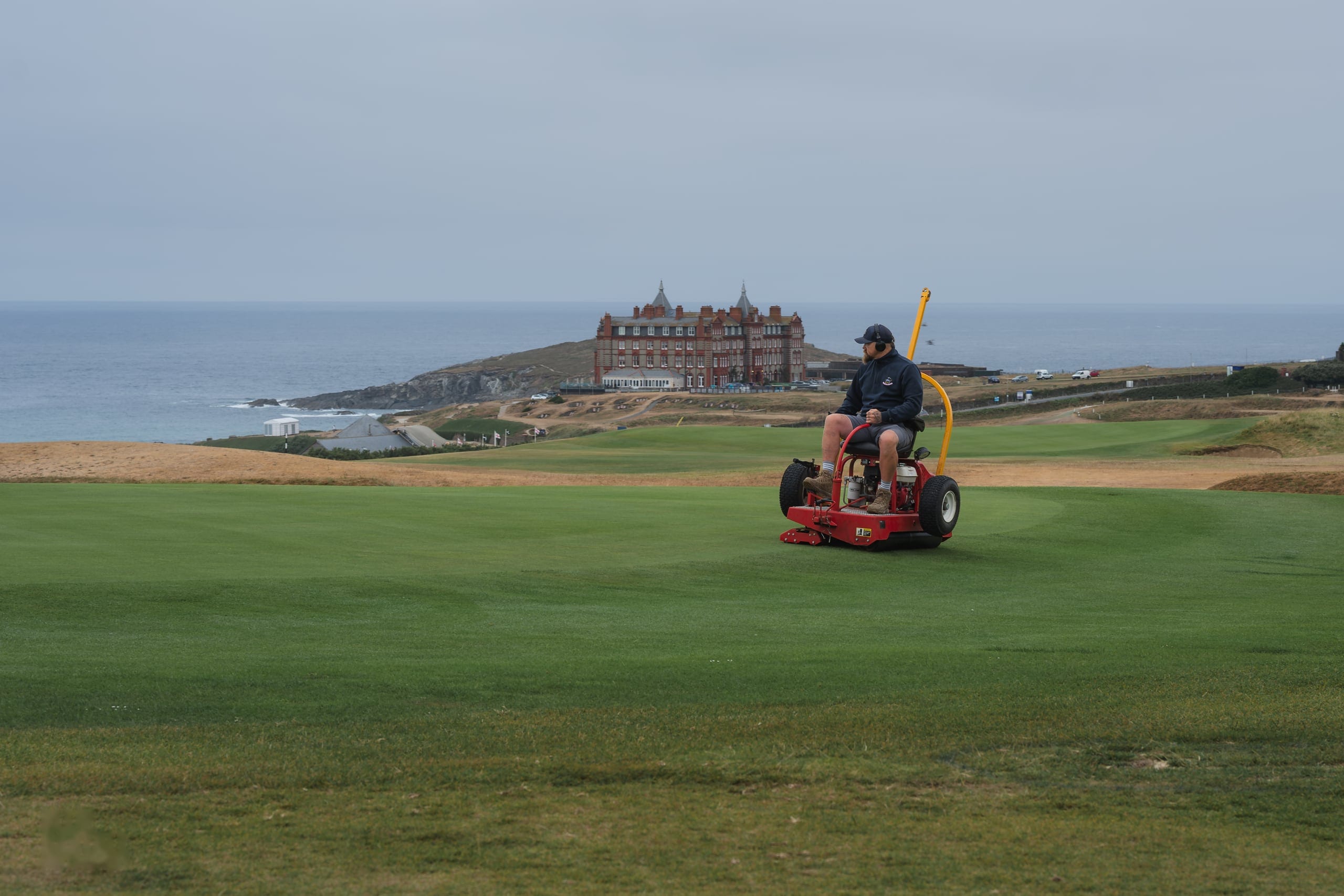 A mower on the links with the headland hotel beyond