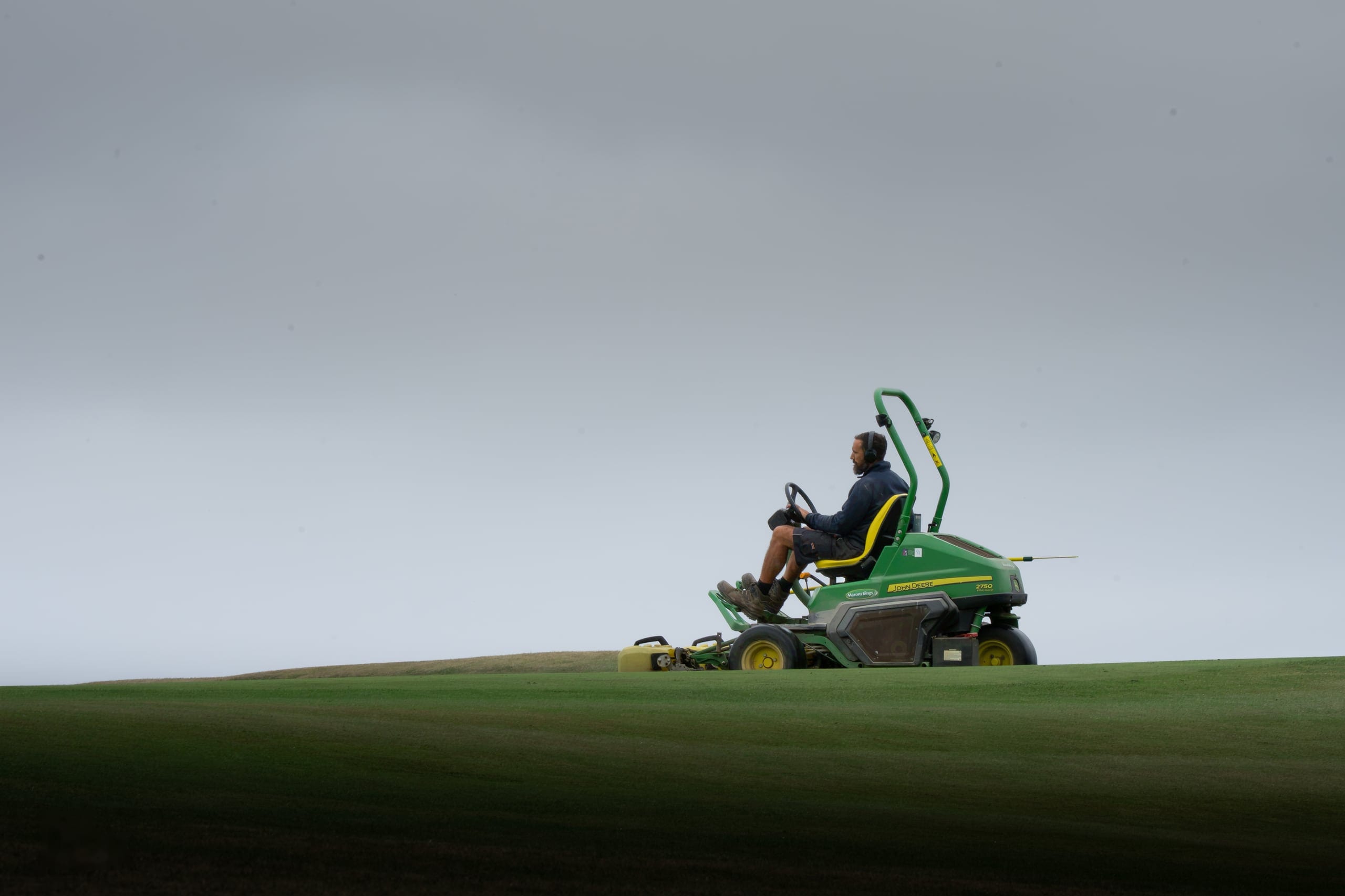 A greenkeeper mowing a green above the sea