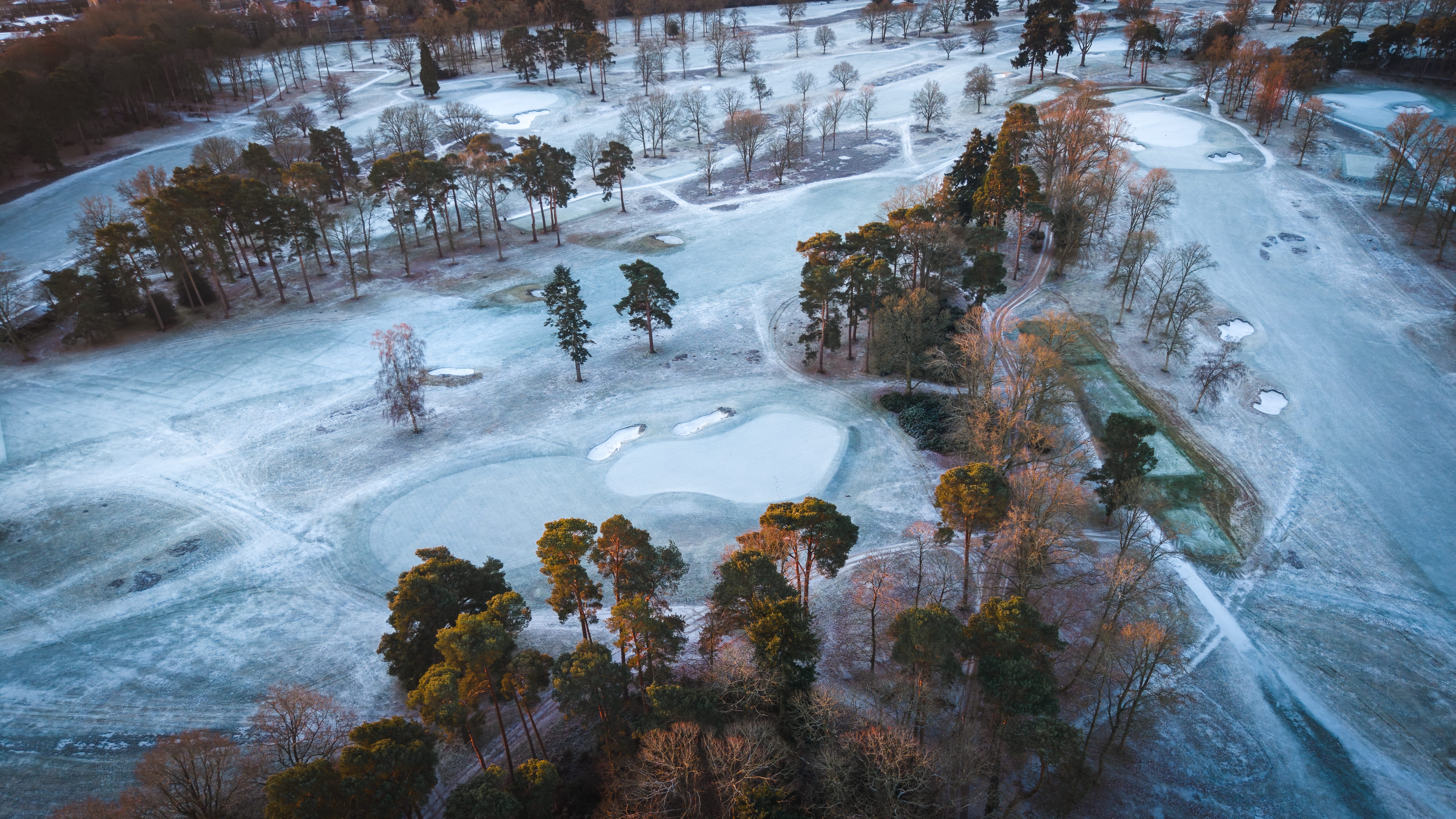 A frosted green and bunkers among pines, low winter sun raking across the fairway