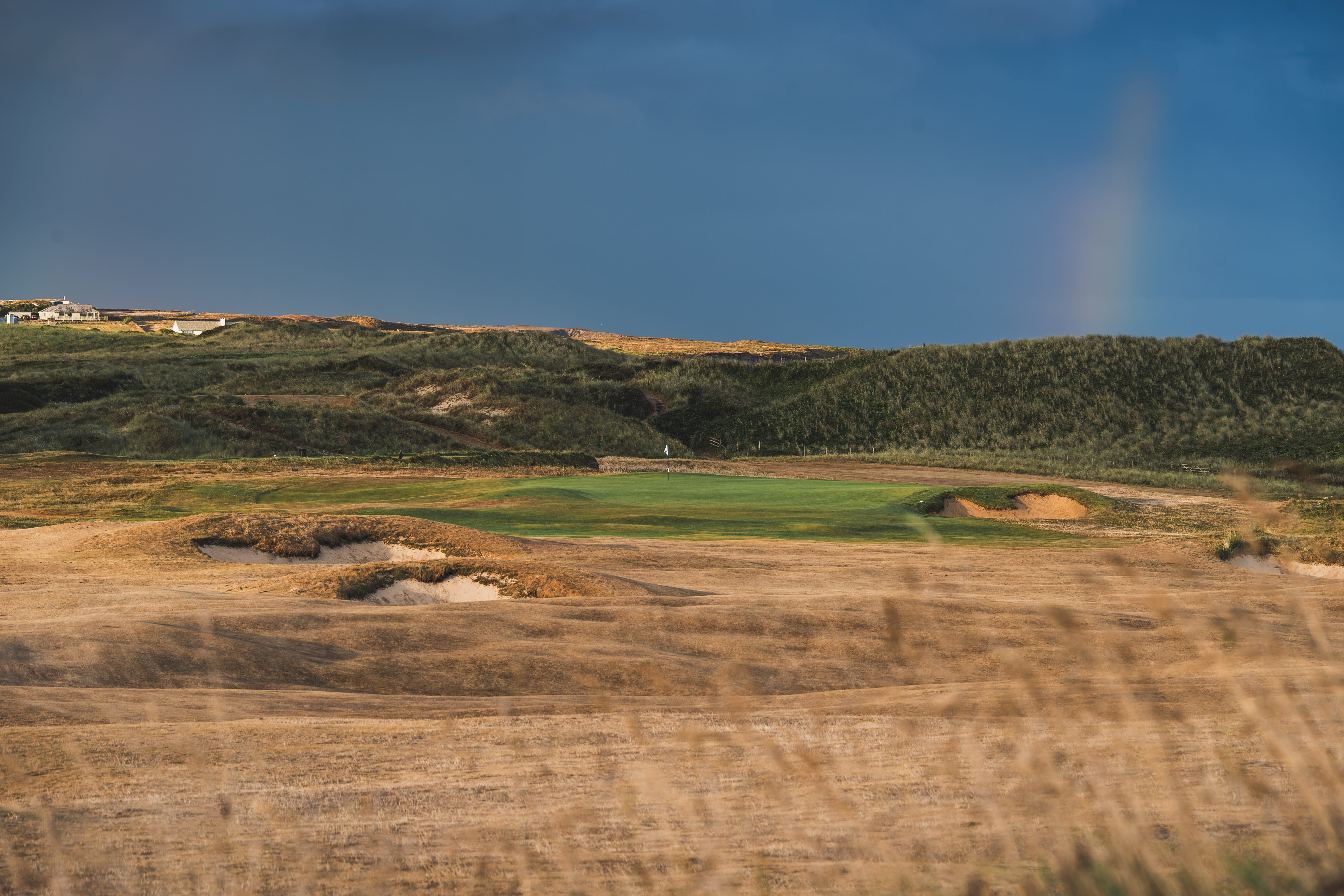 A green tucked among the dunes, storm light over the clubhouse beyond