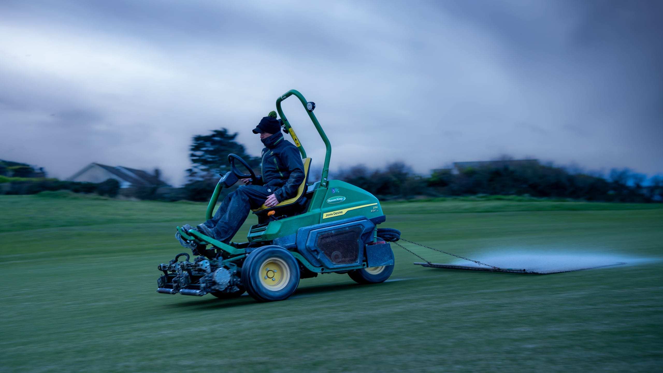 Trevose greenkeeper using a drag mat behind a John Deere mower