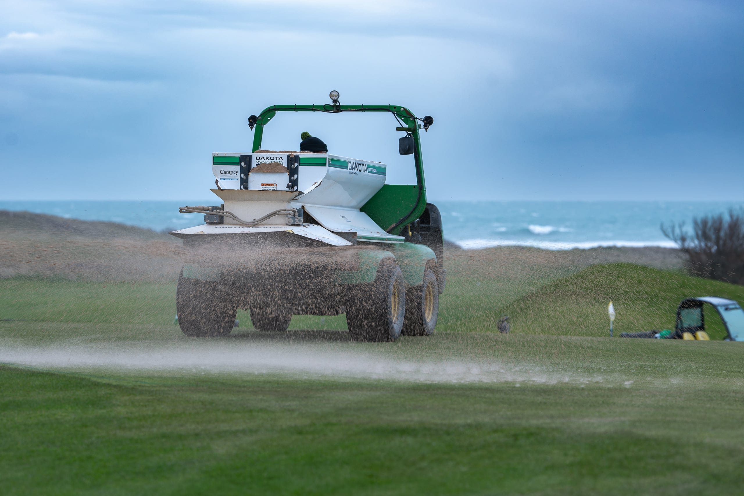 A topdresser working a green beside the sea