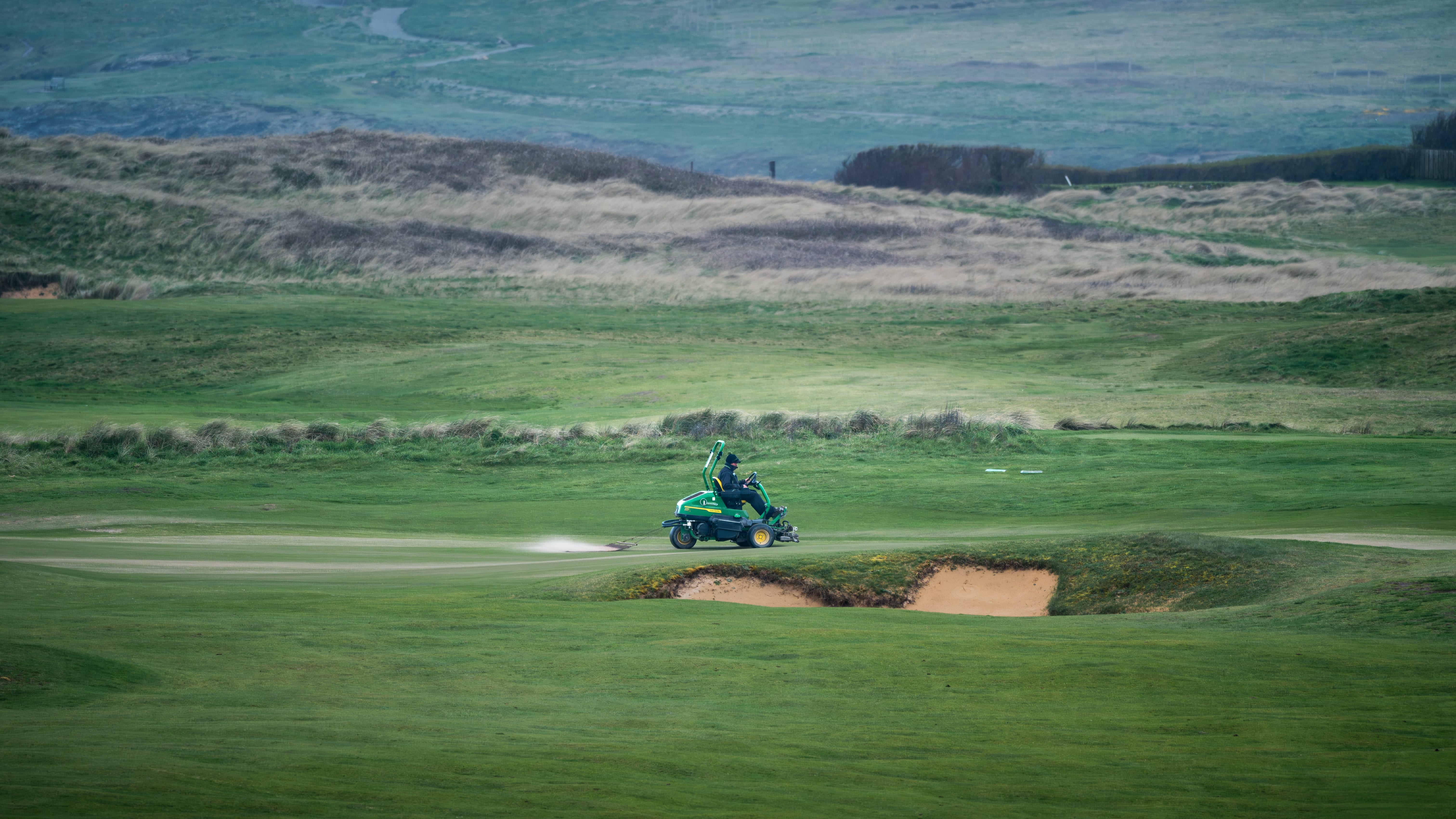 A machine top dressing a green on the links, dunes rolling away behind