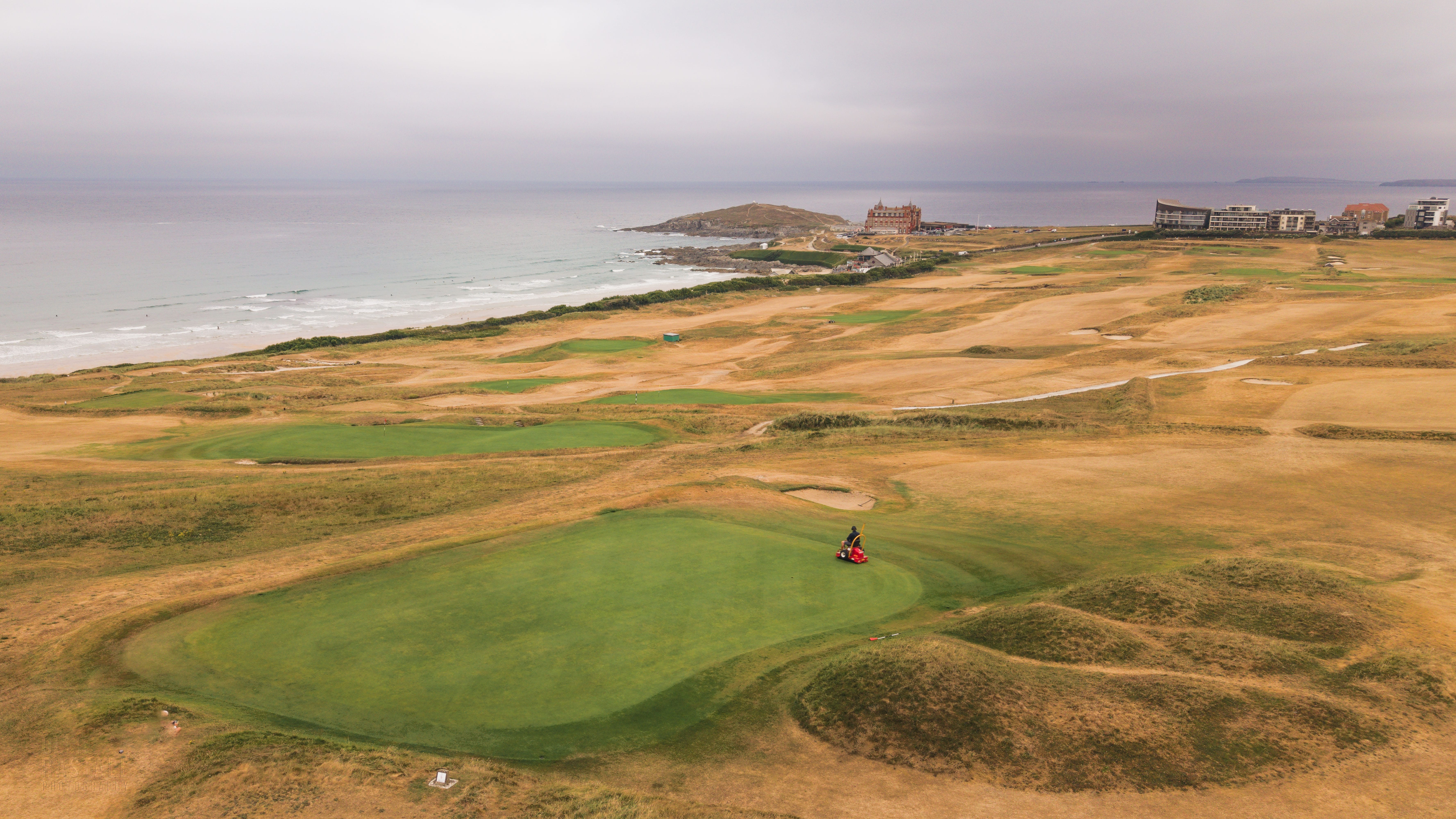 A green on the links at Newquay from the air, a roller working across it